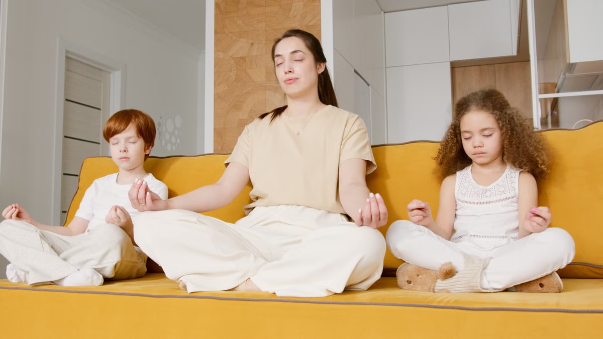 A family enjoying meditation and mindfulness practice together on a yellow couch indoors.